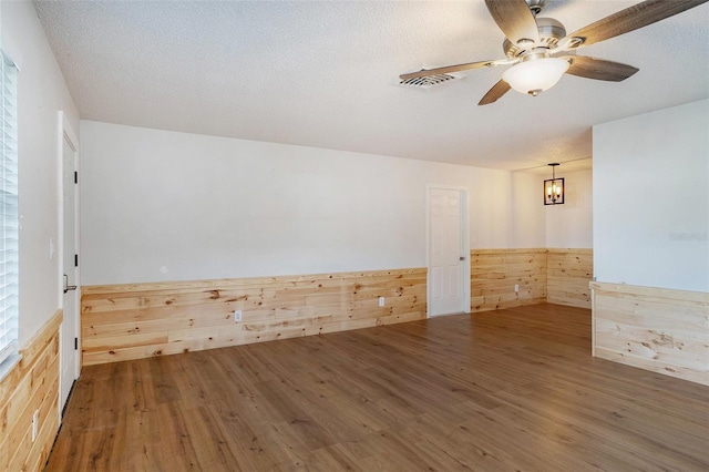 empty room with a textured ceiling, dark hardwood / wood-style flooring, wood walls, and ceiling fan with notable chandelier