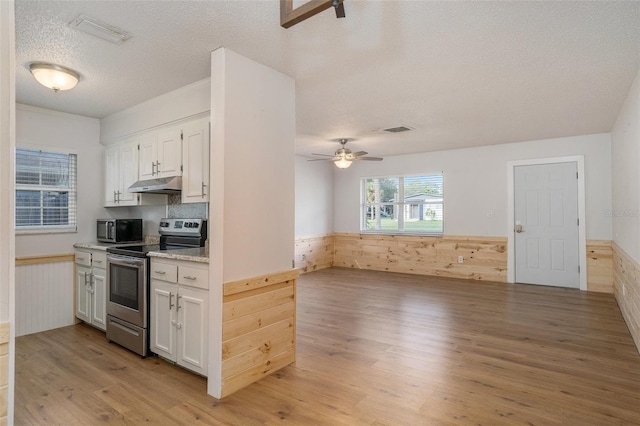 kitchen with ceiling fan, stainless steel appliances, white cabinetry, and wood walls