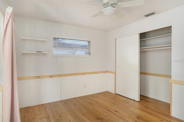 unfurnished bedroom with a closet, wood walls, light wood-type flooring, ceiling fan, and a textured ceiling