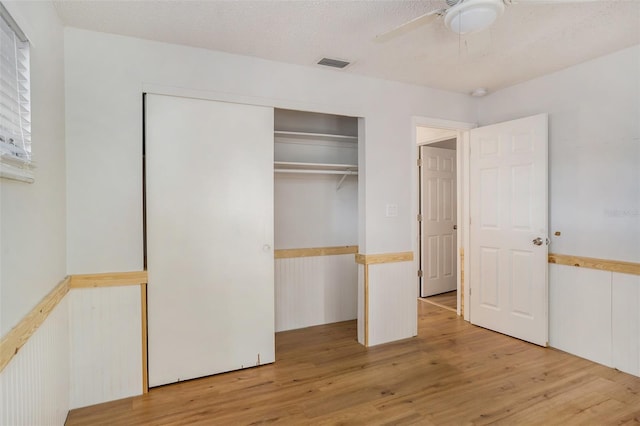 unfurnished bedroom with a textured ceiling, a closet, ceiling fan, and light hardwood / wood-style floors