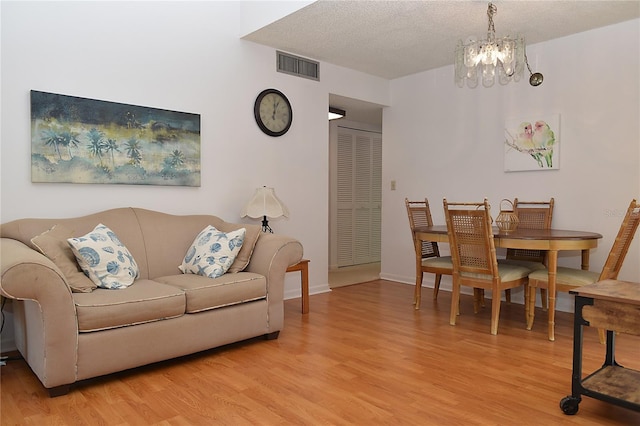 living room with a textured ceiling, a chandelier, and light wood-type flooring