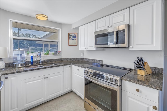 kitchen with stainless steel appliances, white cabinetry, sink, and dark stone counters