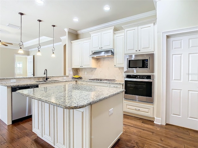 kitchen with dark wood finished floors, stainless steel appliances, ornamental molding, a sink, and under cabinet range hood