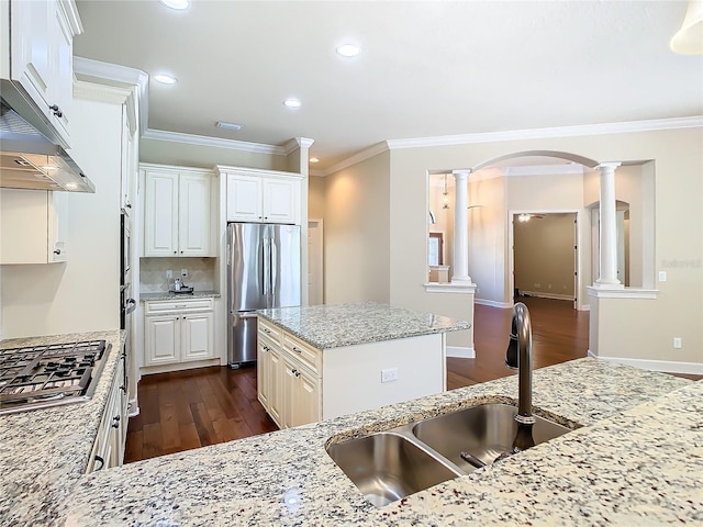 kitchen with arched walkways, a sink, appliances with stainless steel finishes, ornate columns, and crown molding