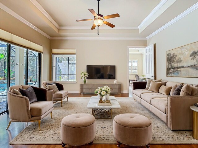 living area with plenty of natural light, a raised ceiling, crown molding, and wood finished floors