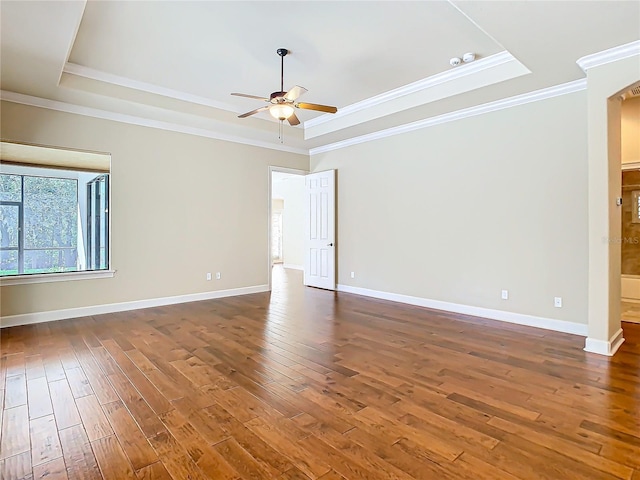 unfurnished room featuring a raised ceiling, dark wood-type flooring, ornamental molding, ceiling fan, and baseboards