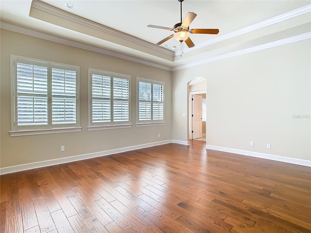 empty room with arched walkways, a raised ceiling, and wood finished floors