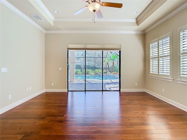 empty room with a raised ceiling, visible vents, ornamental molding, baseboards, and hardwood / wood-style flooring