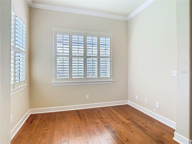 empty room with baseboards, crown molding, and wood finished floors