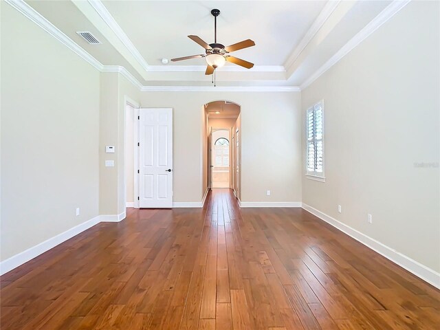 spare room with arched walkways, hardwood / wood-style flooring, visible vents, baseboards, and a tray ceiling