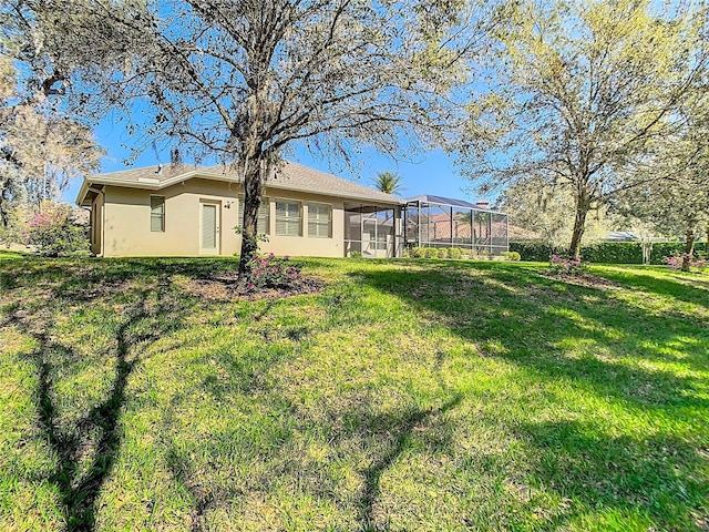 back of house featuring a lanai, a lawn, and stucco siding