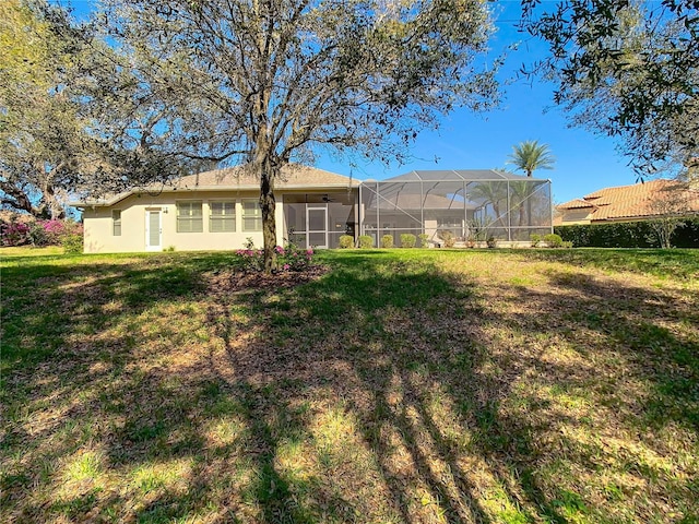 rear view of property featuring glass enclosure, stucco siding, and a yard