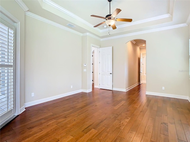 unfurnished room with arched walkways, visible vents, ornamental molding, wood-type flooring, and a raised ceiling