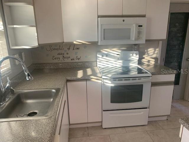 kitchen with white appliances, white cabinets, light tile patterned floors, and sink