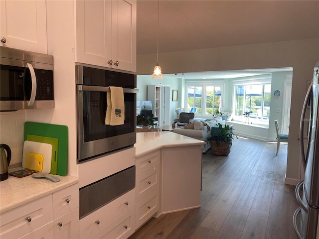 kitchen with light stone counters, dark wood-type flooring, pendant lighting, stainless steel appliances, and white cabinetry