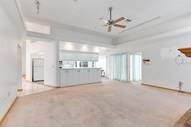 unfurnished living room featuring ceiling fan, rail lighting, light carpet, and a textured ceiling