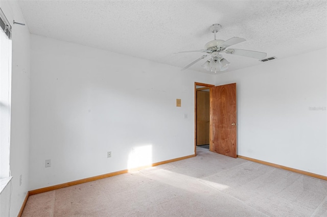 empty room with ceiling fan, light colored carpet, and a textured ceiling