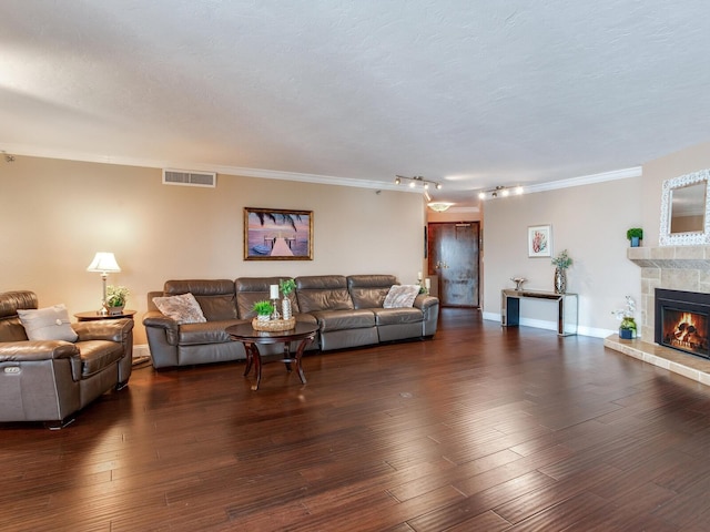 living room with a textured ceiling, track lighting, dark wood-type flooring, a fireplace, and crown molding