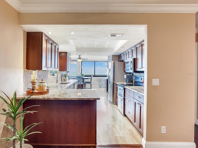 kitchen featuring kitchen peninsula, a tray ceiling, stainless steel appliances, and ornamental molding