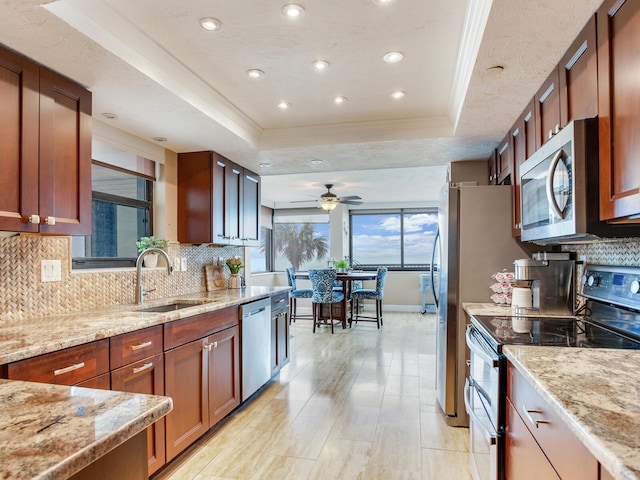 kitchen with ceiling fan, light stone counters, a tray ceiling, and stainless steel appliances