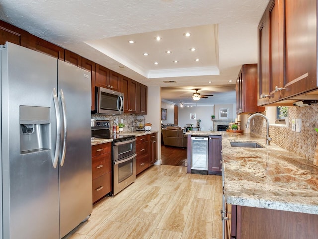 kitchen with stainless steel appliances, wine cooler, sink, ceiling fan, and a tray ceiling