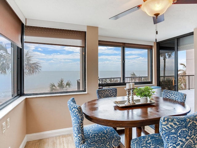 dining area featuring ceiling fan, a wealth of natural light, a water view, and wood-type flooring