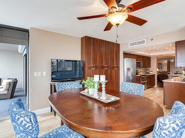 dining area featuring ceiling fan, a tray ceiling, and light hardwood / wood-style flooring