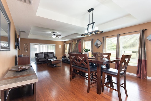 dining space with dark wood-type flooring, ceiling fan, and a tray ceiling