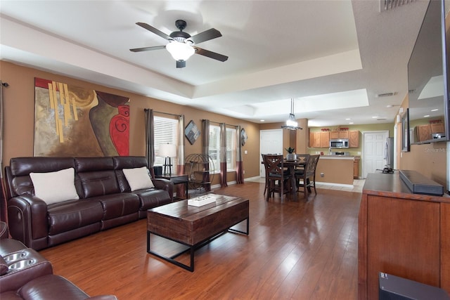 living room featuring a raised ceiling, ceiling fan, and dark hardwood / wood-style floors