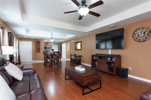 living room with ceiling fan, a raised ceiling, and wood-type flooring