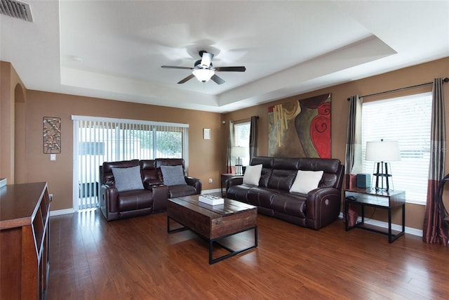 living room featuring dark wood-type flooring, ceiling fan, and a tray ceiling