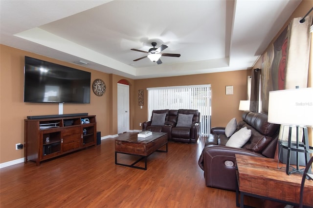 living room with ceiling fan, a tray ceiling, and dark wood-type flooring