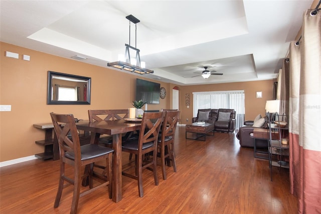 dining space featuring dark hardwood / wood-style flooring, a raised ceiling, and ceiling fan