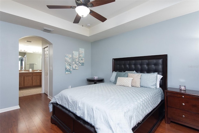 bedroom with wood-type flooring, ensuite bath, ceiling fan, and a raised ceiling