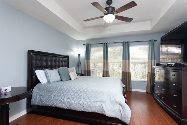 bedroom with a raised ceiling, ceiling fan, multiple windows, and dark hardwood / wood-style floors