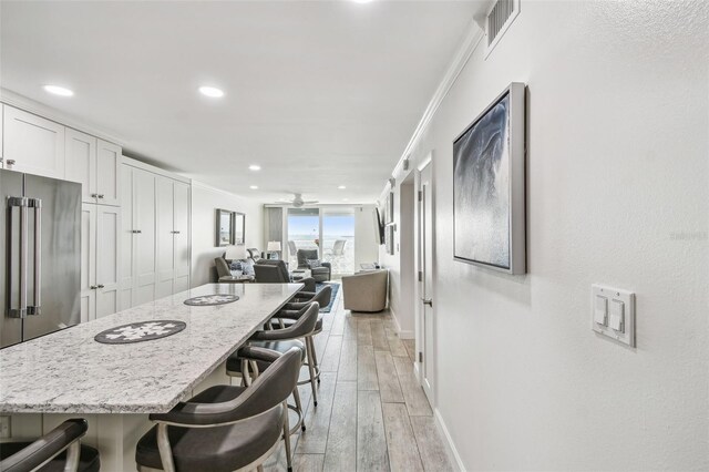 kitchen featuring a center island, a kitchen bar, light stone counters, high end refrigerator, and white cabinets