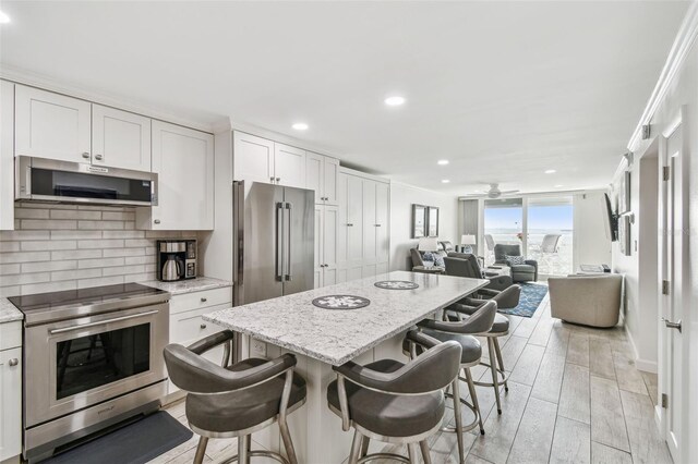 kitchen featuring decorative backsplash, a kitchen island, appliances with stainless steel finishes, open floor plan, and wood finish floors