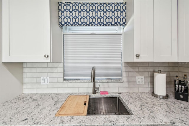 kitchen featuring light stone counters, backsplash, a sink, and white cabinetry