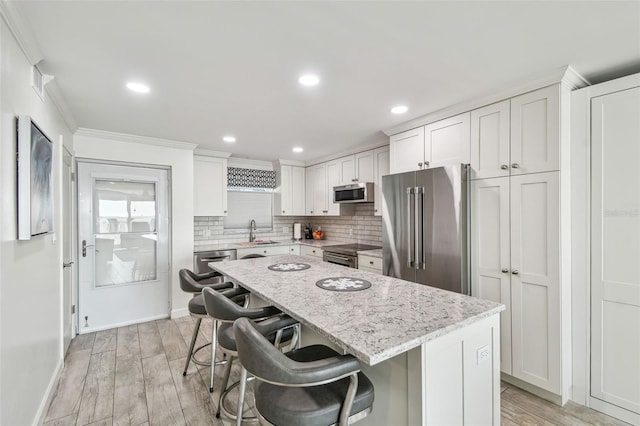 kitchen with light wood-style flooring, stainless steel appliances, a sink, backsplash, and a center island