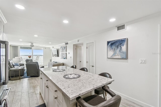 kitchen featuring light wood-style floors, visible vents, crown molding, and a breakfast bar area