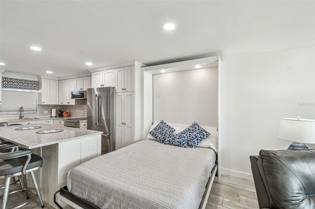 bedroom with light wood-style floors, high end refrigerator, a sink, and recessed lighting