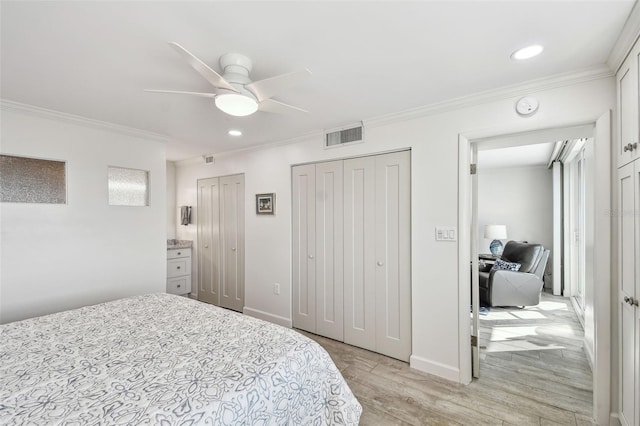 bedroom with visible vents, baseboards, ornamental molding, light wood-type flooring, and two closets