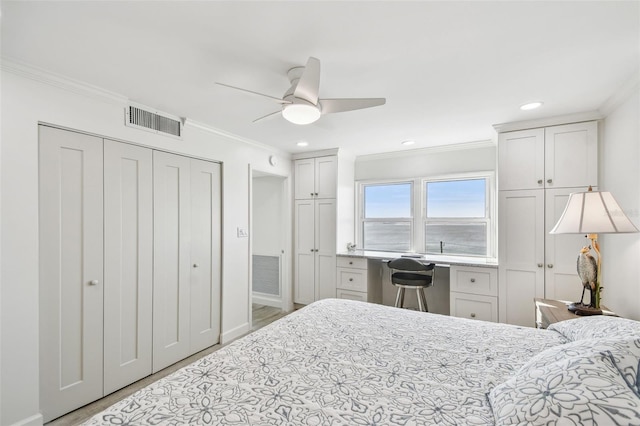 bedroom with ornamental molding, built in desk, two closets, and visible vents