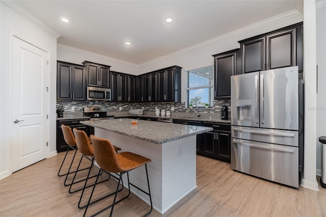 kitchen featuring appliances with stainless steel finishes, a kitchen island, dark stone countertops, decorative backsplash, and a breakfast bar area