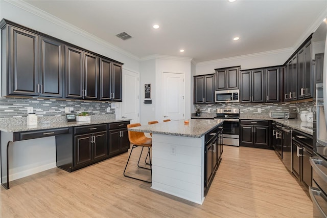 kitchen featuring appliances with stainless steel finishes, a kitchen island, light hardwood / wood-style flooring, crown molding, and a breakfast bar area