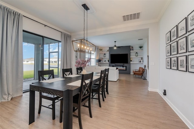 dining room with ceiling fan with notable chandelier, built in features, crown molding, a water view, and light hardwood / wood-style flooring