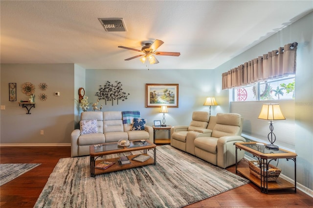 living room with dark wood-type flooring, ceiling fan, and a textured ceiling