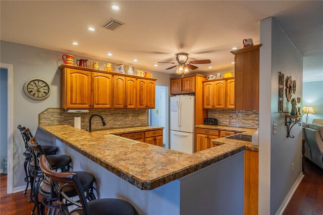 kitchen with dark hardwood / wood-style floors, a kitchen breakfast bar, decorative backsplash, white refrigerator, and kitchen peninsula