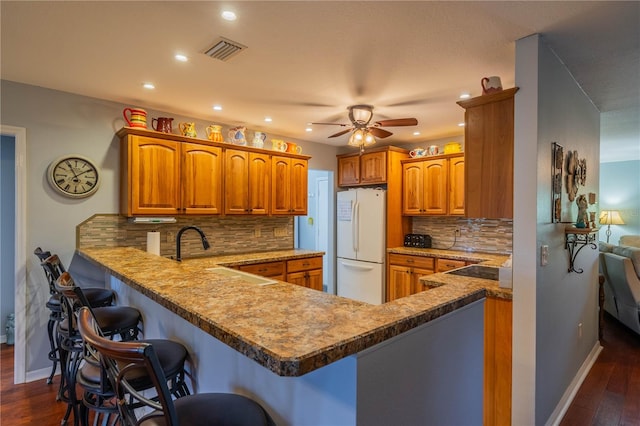 kitchen with tasteful backsplash, a kitchen bar, white fridge, kitchen peninsula, and dark wood-type flooring