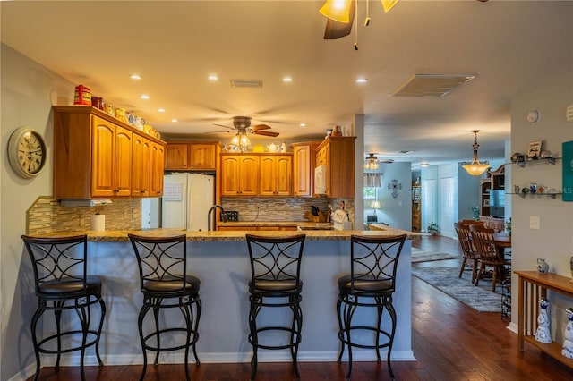 kitchen with a breakfast bar, dark hardwood / wood-style floors, kitchen peninsula, white appliances, and backsplash